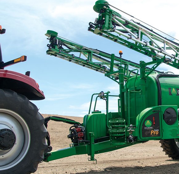 Side view of red tractor towing green spray trailer